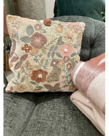 Coussin floral brodé exposé sur sur un fauteuil avec un plaid pour une décoration de salon bohème chic.