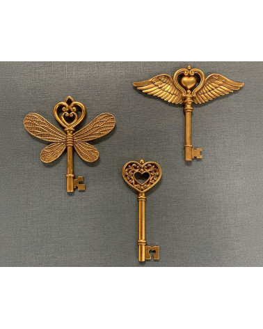 Trio de clés murales décoratives dorées de différentes tailles en résine, incluant la clé ailes cœur et la clé papillon.