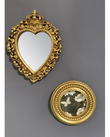 Miroir baroque doré en forme de cœur accroché sur un mur gris, accompagné d’un cadre rond décoratif