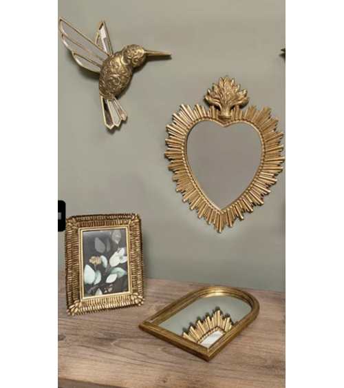 Mise en scène intérieure d'un colibri mural doré associé à un miroir cœur et un cadre baroque sur un mur vert olive.