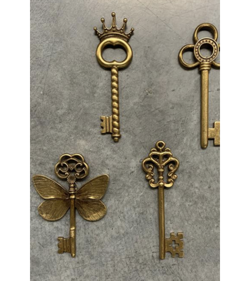 Composition murale de clés décoratives dorées de différentes formes, incluant la clé ailée et la clé couronne.