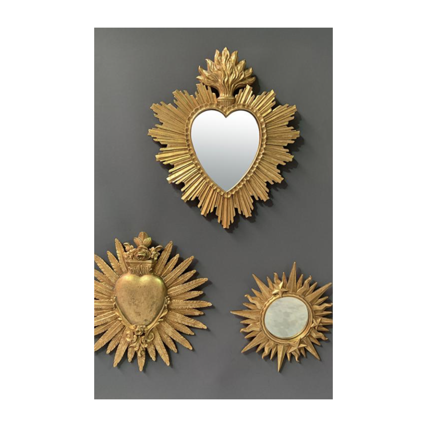 Trio de décorations murales dorées incluant un miroir cœur soleil, un ex-voto cœur enflammé et un miroir étoile.