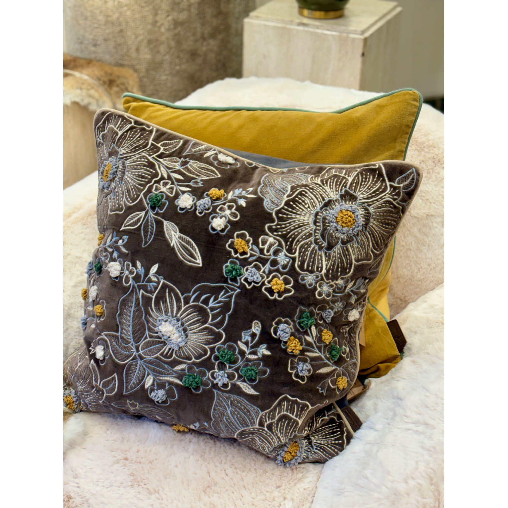 Ambiance cocooning avec un grand coussin gris anthracite brodé posé sur un plaid en fourrure blanche.