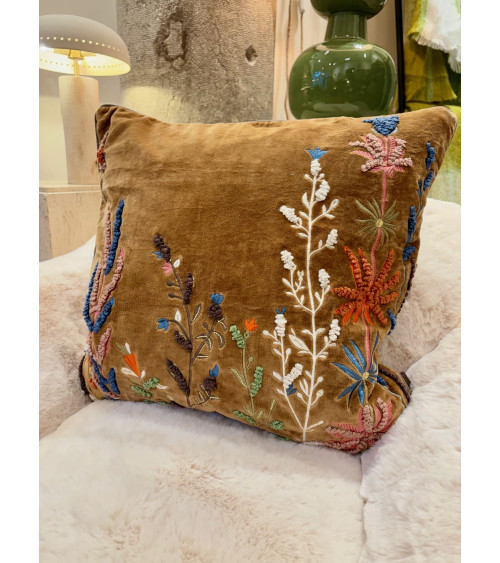 Décoration de salon bohème chic avec une housse de coussin brodée posée sur un canapé en fausse fourrure.