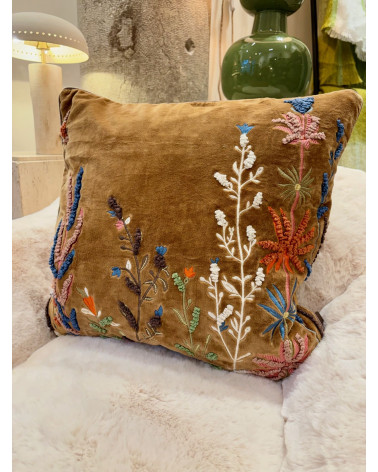 Décoration de salon bohème chic avec une housse de coussin brodée posée sur un canapé en fausse fourrure.