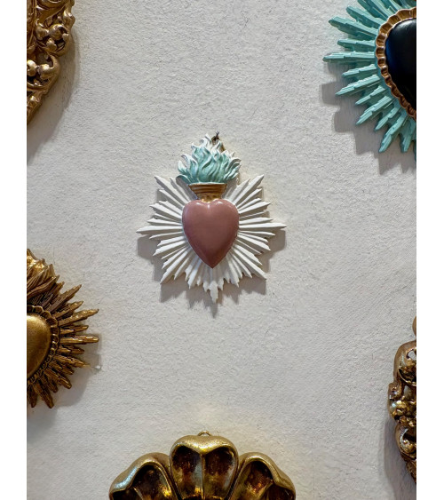 Accumulation d'ex-votos et cœurs sacrés sur un mur blanc pour une décoration de style cabinet de curiosités.