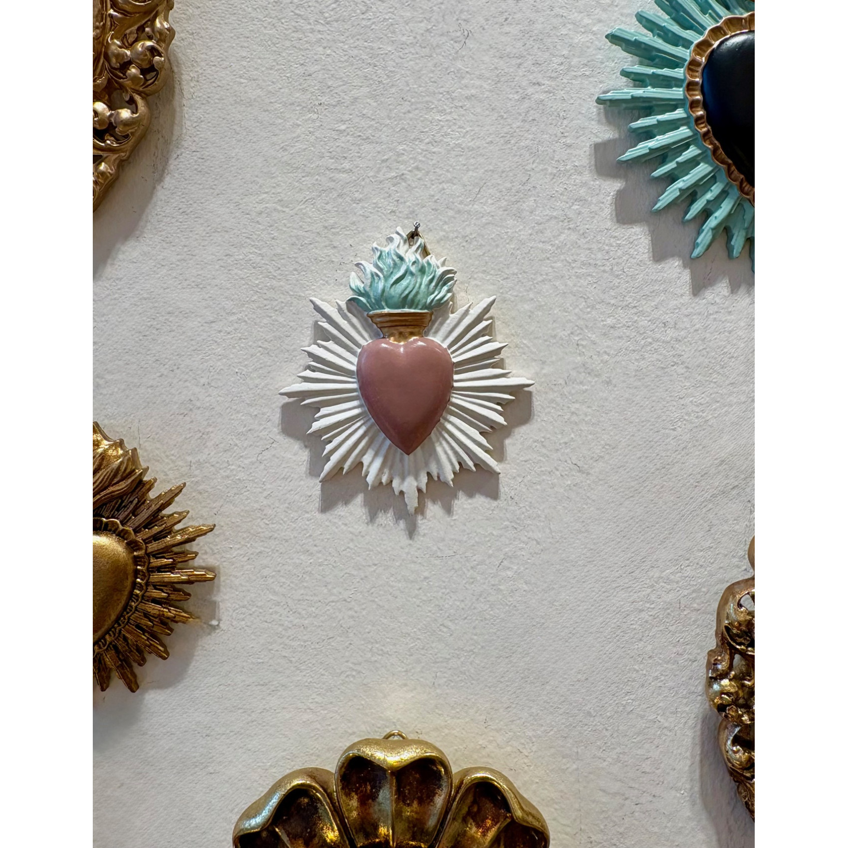 Accumulation d'ex-votos et cœurs sacrés sur un mur blanc pour une décoration de style cabinet de curiosités.