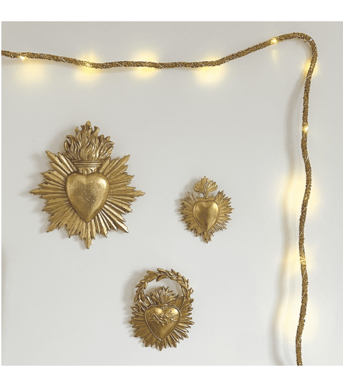 Décoration murale avec cœurs ex-voto dorés style religieux entourés d’une guirlande lumineuse chaleureuse sur mur blanc
